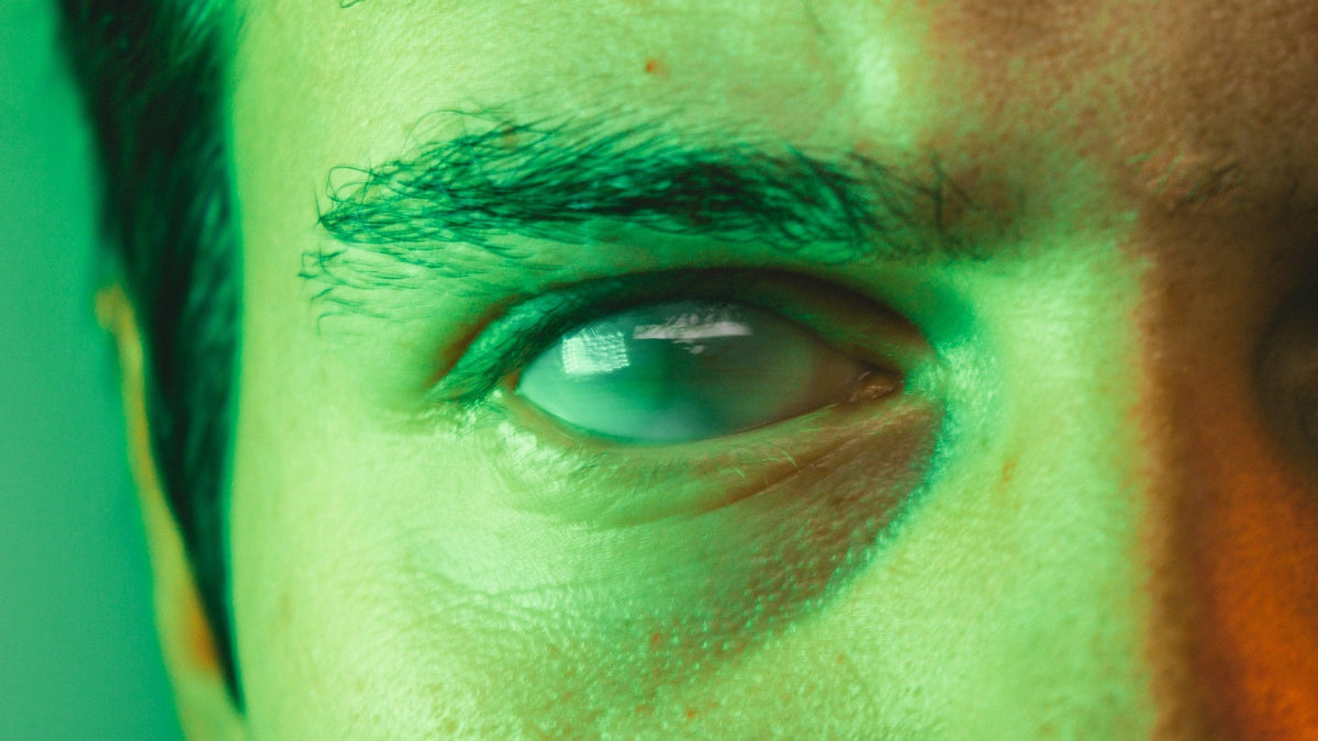 Extreme close-up of a human eye in green and amber light, a window reflected in the iris