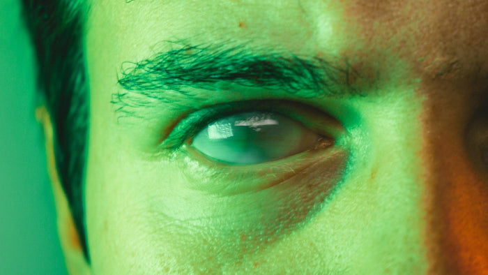 Extreme close-up of a human eye in green and amber light, a window reflected in the iris