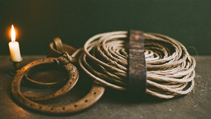 Two weathered horseshoes and a coil of braided cord beside a burning candle on a dark stone surface