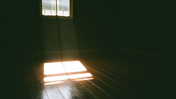 A bright square of afternoon sunlight with the shadow of window bars lying across dark floorboards