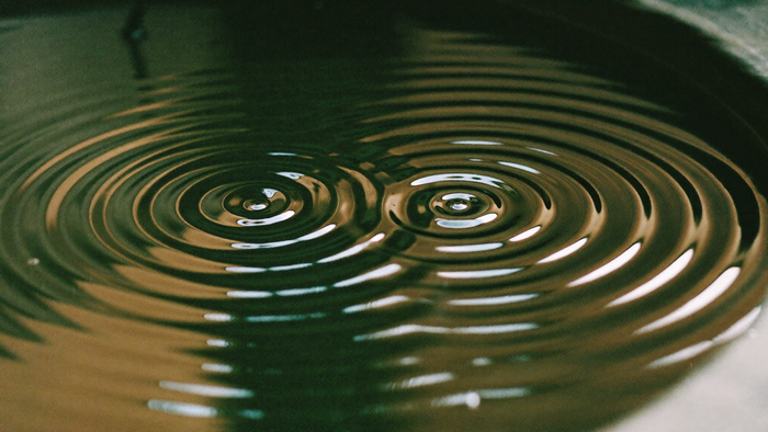 Two sets of concentric ripples spreading across dark water in a stone basin and overlapping where they meet