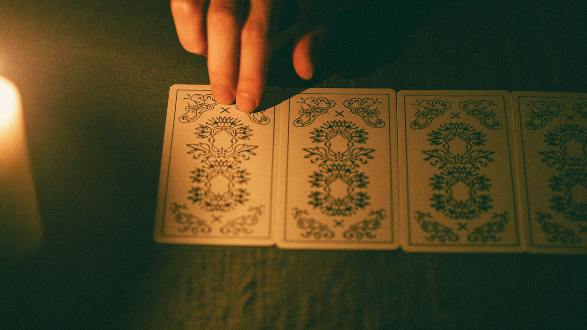 Hand placing a face-down tarot card onto a row of cards already laid out on dark linen by candlelight