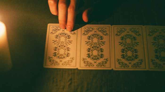 Hand placing a face-down tarot card onto a row of cards already laid out on dark linen by candlelight