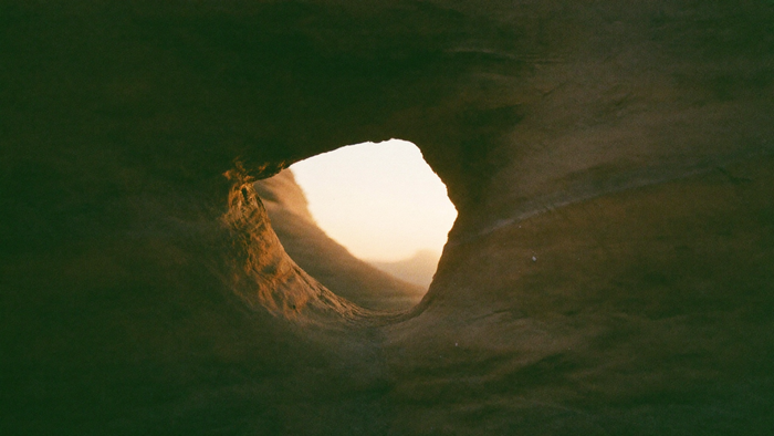 Round opening through a weathered sandstone wall with warm dawn light falling through it