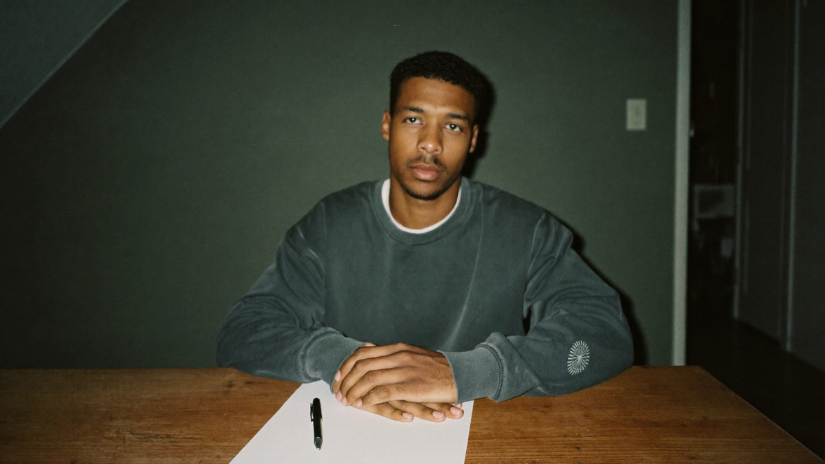 Young man sitting at a bare wooden table with a blank sheet of paper and a pen before a ritual