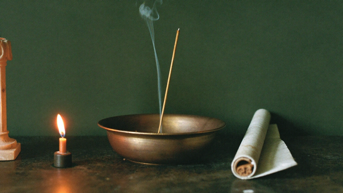 Bronze offering bowl with a burning incense stick, a lit taper and a rolled papyrus scroll on stone