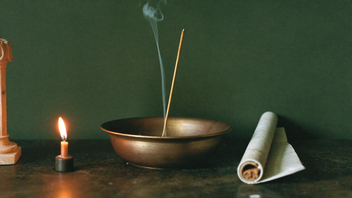 Bronze offering bowl with a burning incense stick, a lit taper and a rolled papyrus scroll on stone