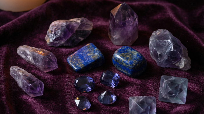Amethyst points, lapis lazuli and fluorite arranged on deep purple velvet beside a burning candle