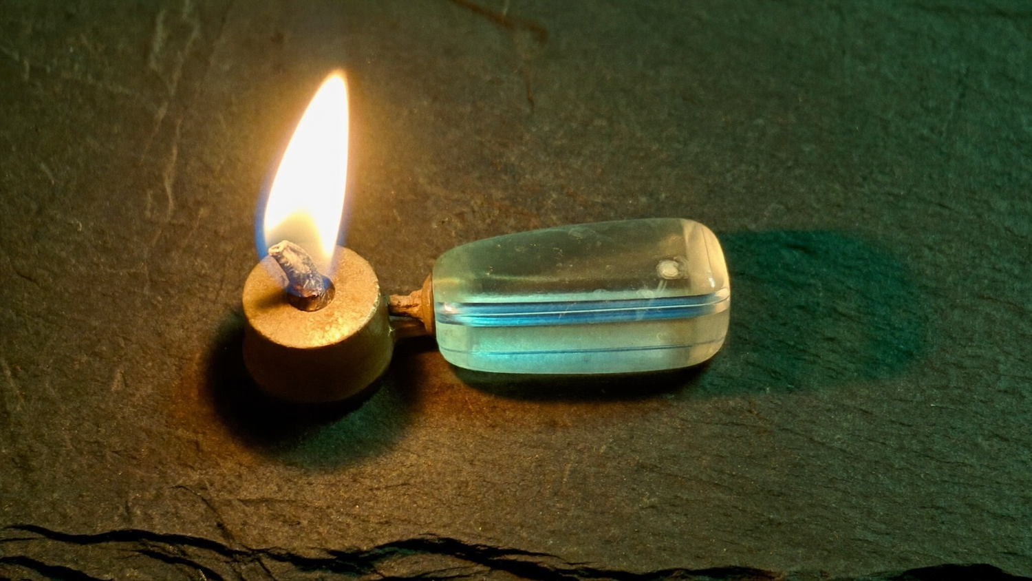 Pale blue banded agate stone resting on dark slate beside a small warm candle flame