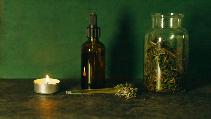 Amber dropper bottle and an apothecary jar of herbs macerating beside a lit tea light