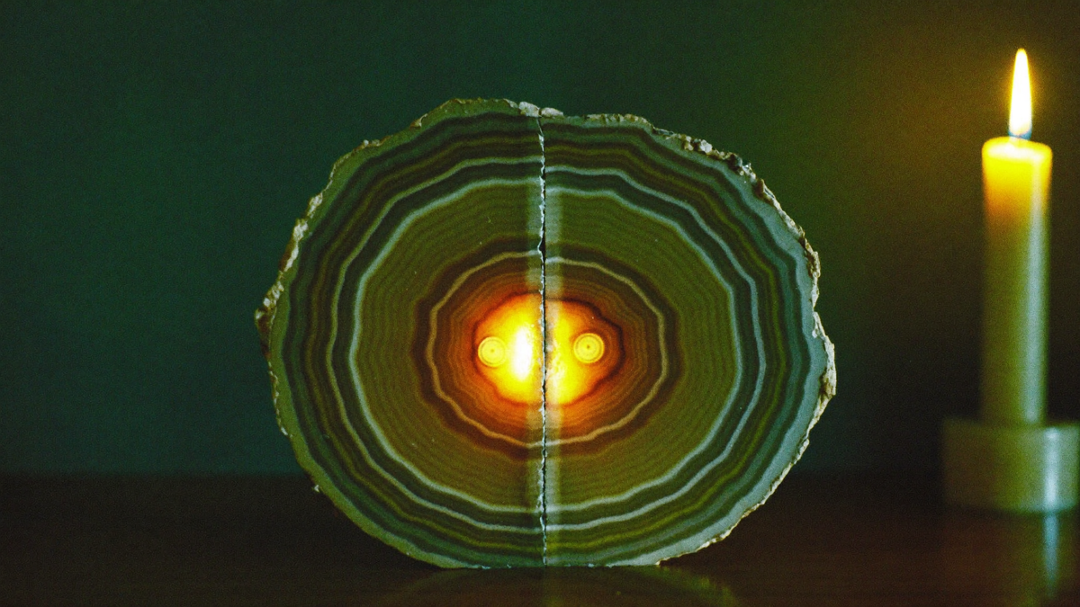 Two halves of a banded agate set back together on dark wood, the seam glowing where candlelight passes through