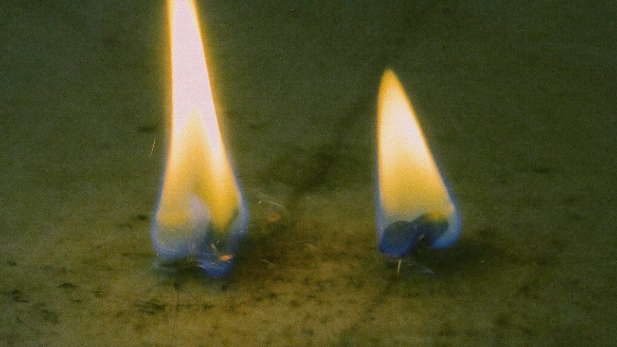 Two separate candle flames on dark stone with a gap between them, one burning tall and steady, the other low