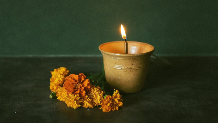 A small clay oil lamp burning beside a handful of orange marigold flowers on a dark stone surface