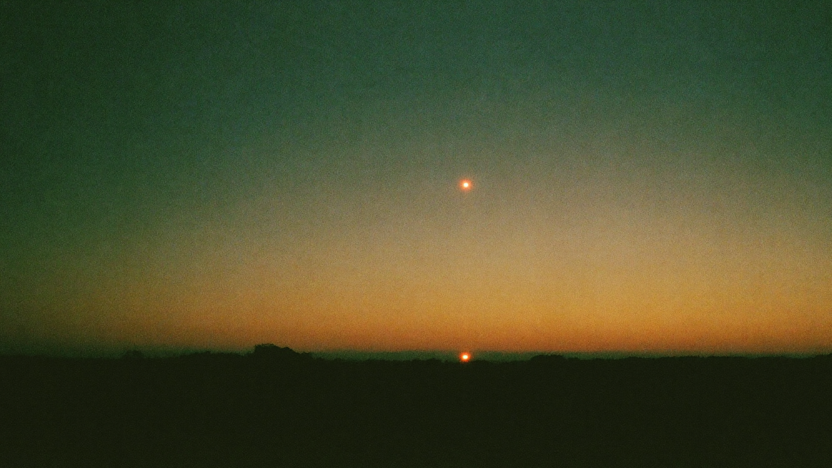 A single bright point of light in a green and amber twilight sky above a dark low horizon