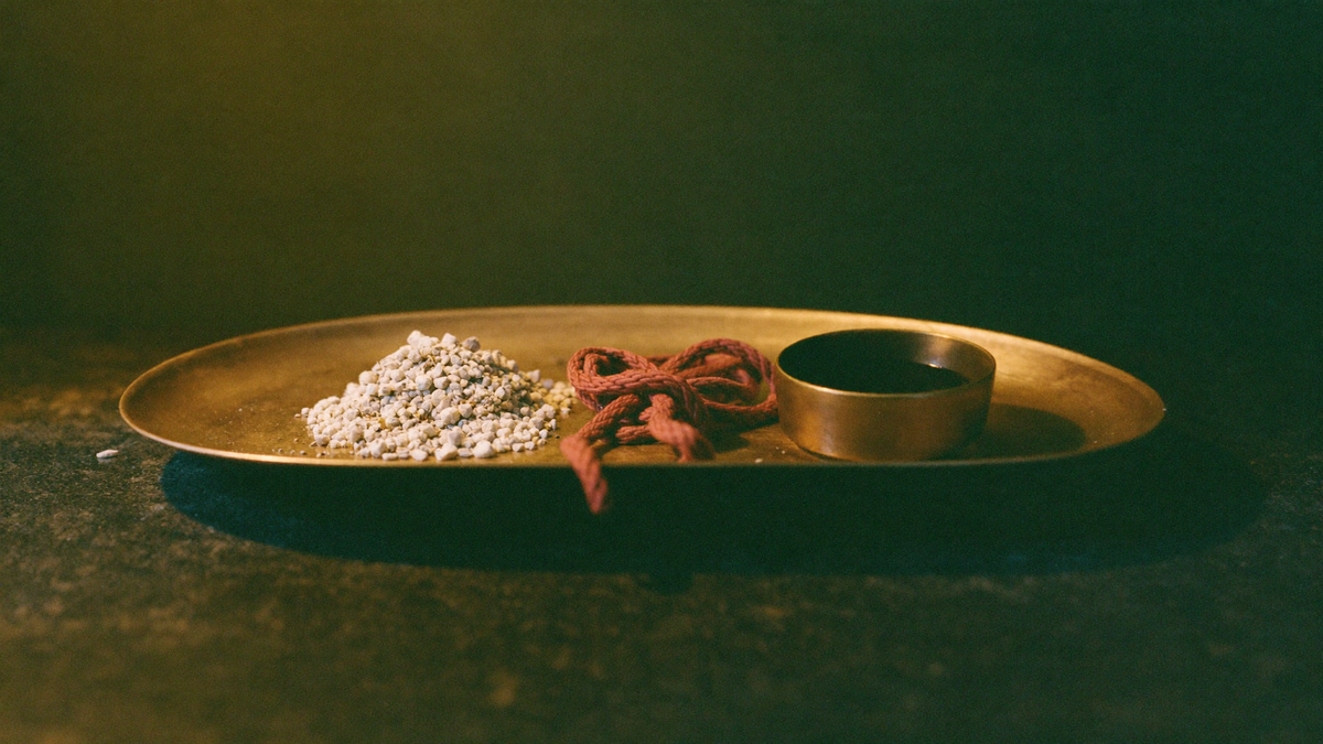 Brass tray holding pale ash, a knotted red cord and cooled dark wax after a completed ritual working