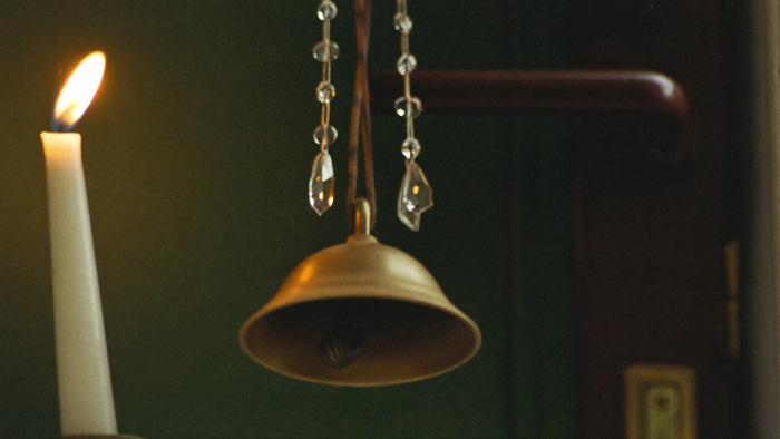A brass witch bell with crystal charms hanging from a dark wooden door handle by candlelight