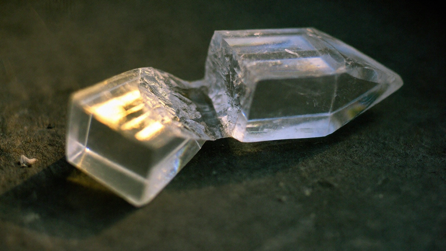 Macro close-up of a clear quartz crystal point split into two halves on dark stone in warm candlelight