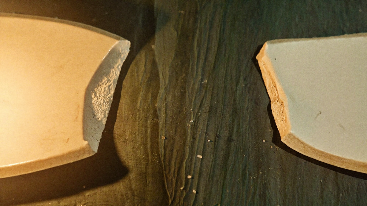 Two broken halves of a ceramic ritual bowl resting on a dark green stone surface in warm candlelight