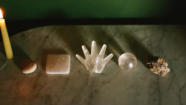 Five forms of pale quartz in a row on marble by candlelight: pebble, palm stone, cluster, sphere and raw chunk