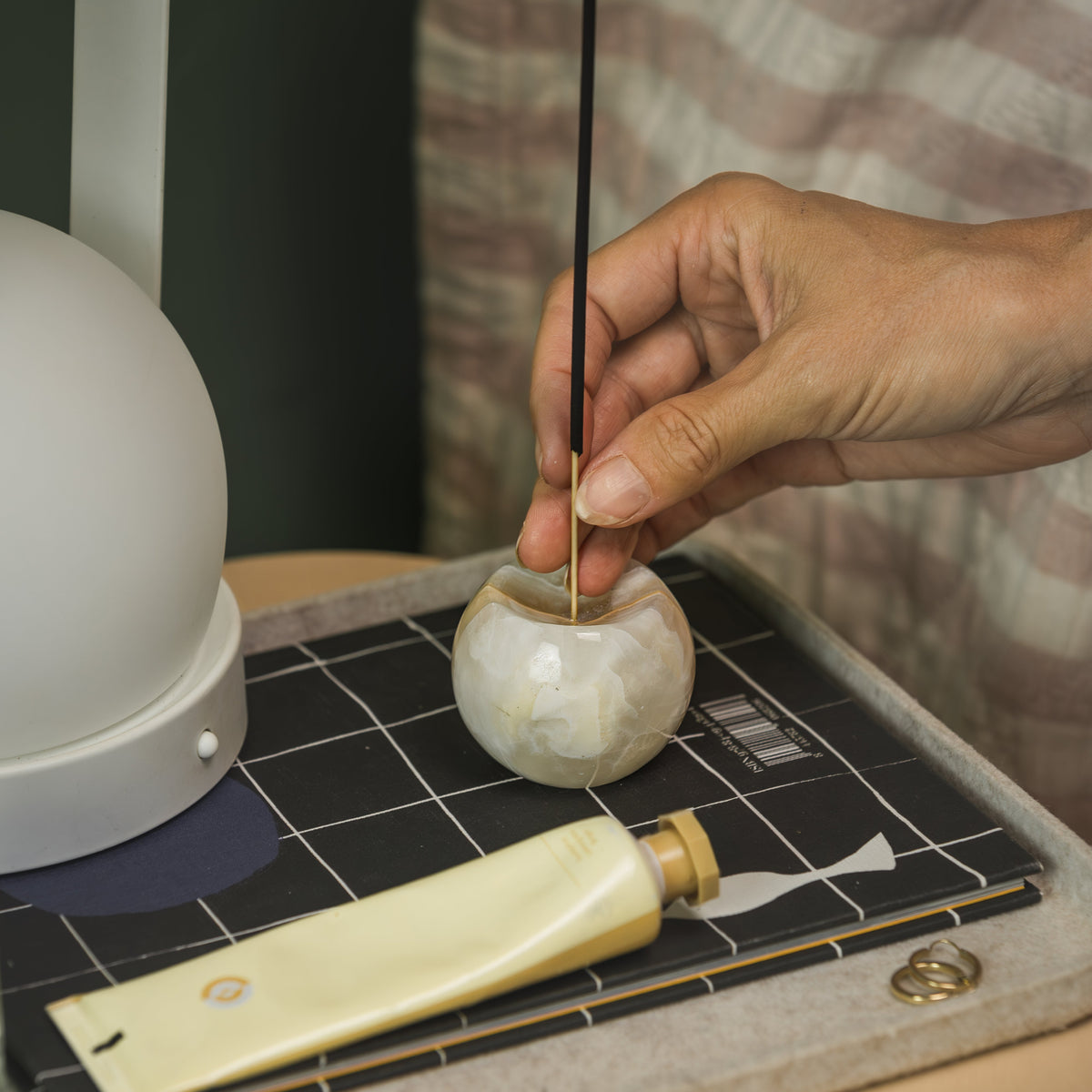 Hand setting an incense stick into the cream onyx sphere holder on a desk tray