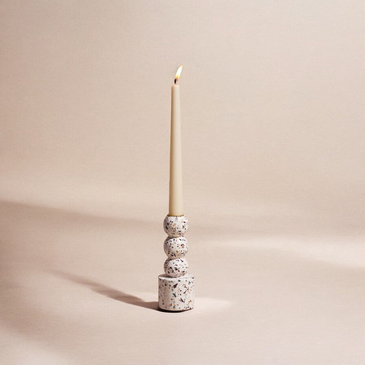 Small Centro terrazzo candle holder with a lit taper, seen against a soft blush backdrop
