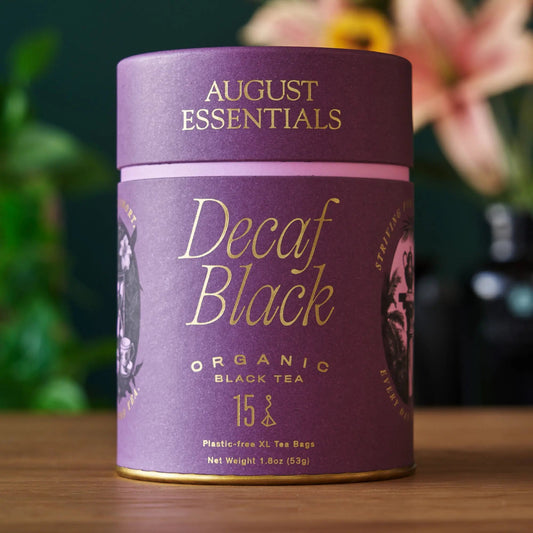 A purple August Essentials carton of Decaf Black organic black tea, 15 tea bags, on a wooden surface.
