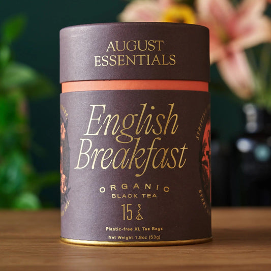 A brown August Essentials carton of English Breakfast organic black tea, 15 tea bags, on a wooden surface.