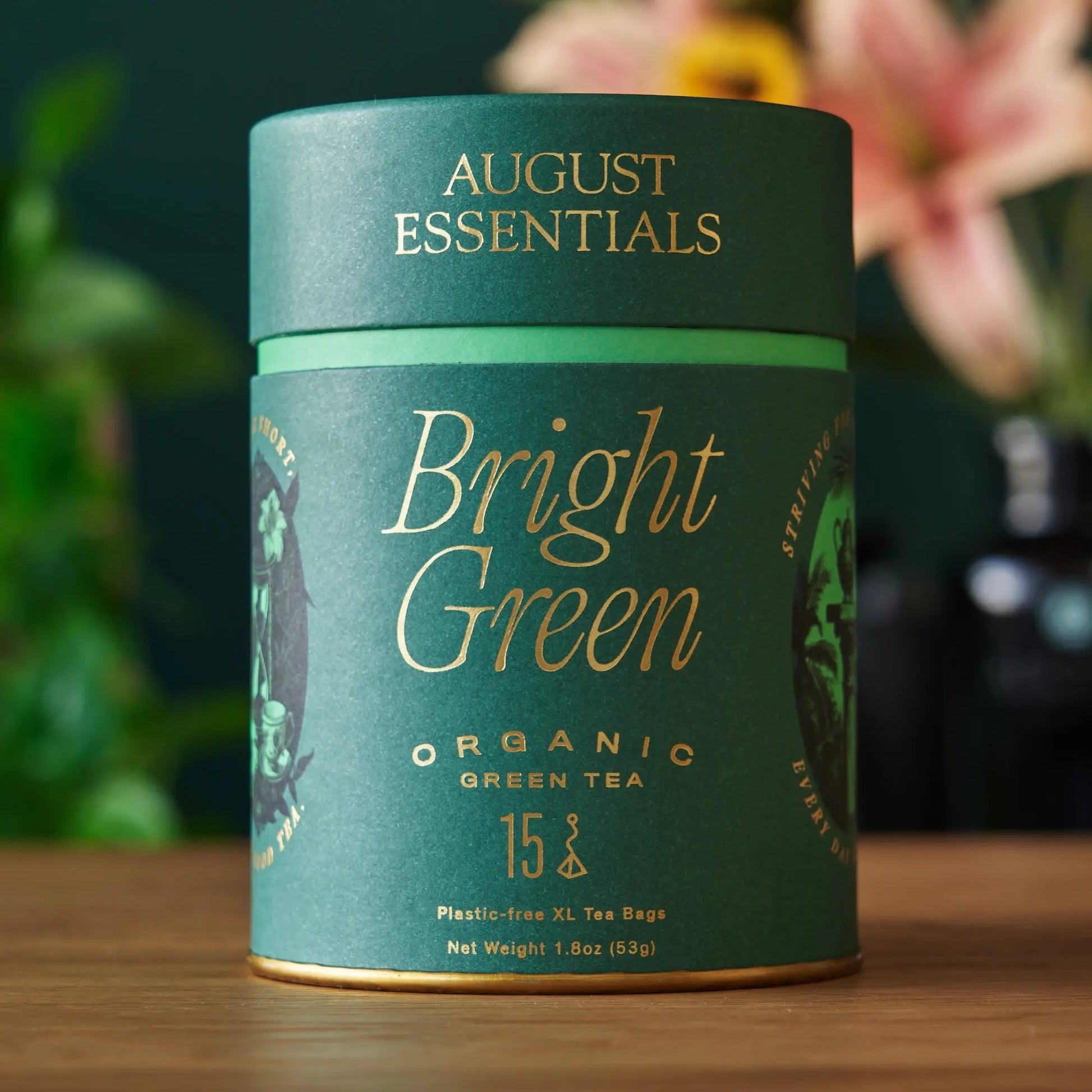 A teal August Essentials carton of Bright Green organic green tea, 15 tea bags, standing on a wooden surface.