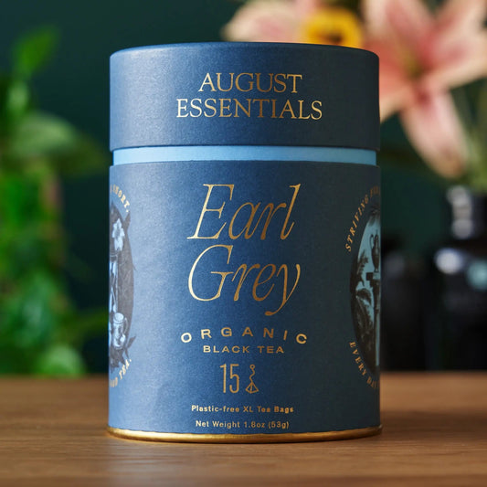 A blue August Essentials carton of Earl Grey organic black tea, 15 tea bags, on a wooden surface.