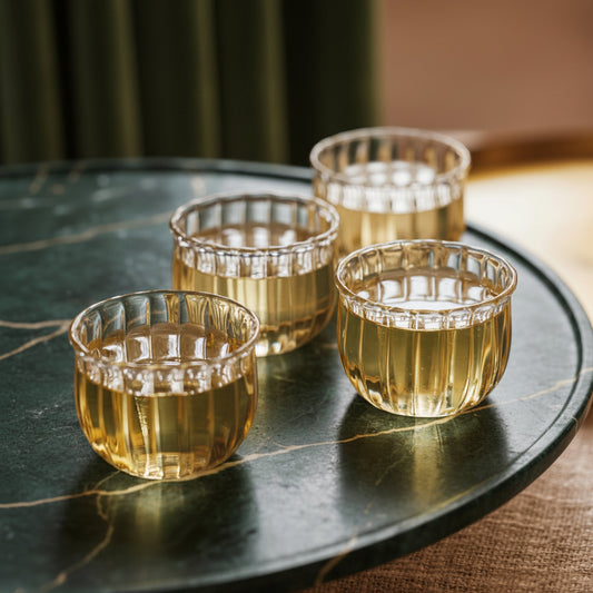 Four Kira glass cups filled with tea on a dark green marble tray