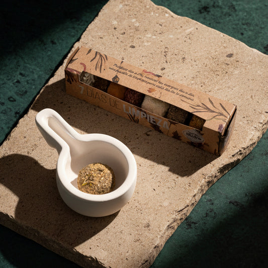 Seven-day charcoal tablet box open on a stone slab beside a white ceramic burner holding one herb-topped disc
