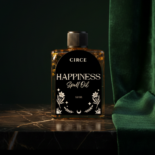 The Happiness spell oil bottle on dark marble beside green velvet, its arched black label reading 'Circe - Happiness Spell Oil, 1/2 oz.'