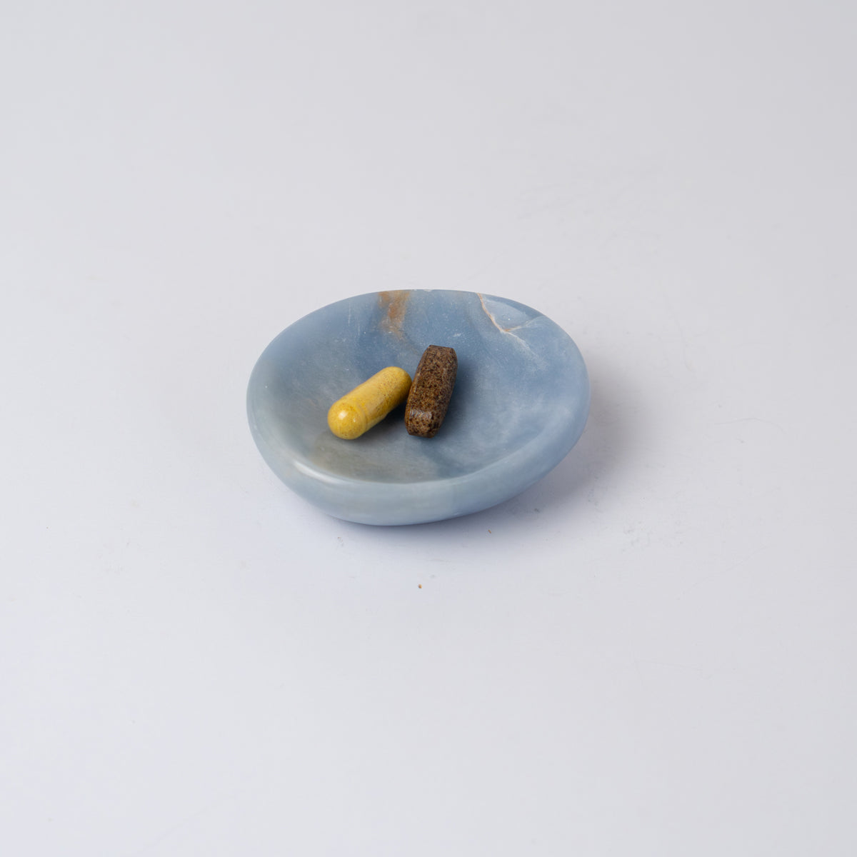 Angelite dish holding two capsules, showing the natural veining through the stone