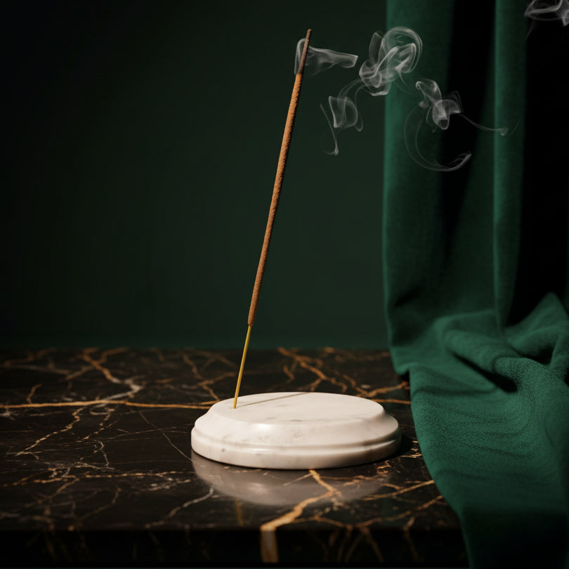 White marble incense holder catching ash on a dark marble surface, incense smoking