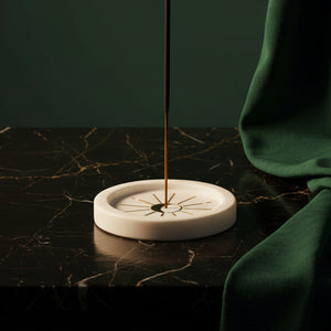 Round white marble incense holder with brass moon and ray inlay on dark marble, stick burning