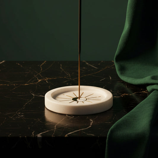 Round white marble incense holder with brass moon and ray inlay on dark marble, stick burning