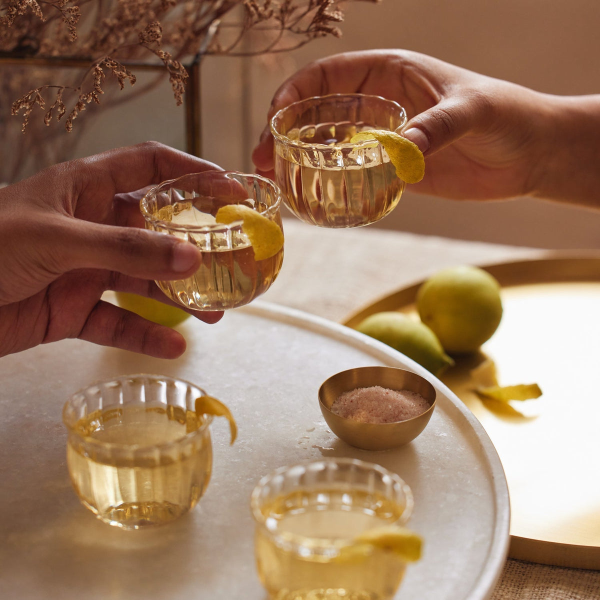 Two hands lifting Kira glass cups garnished with lemon peel
