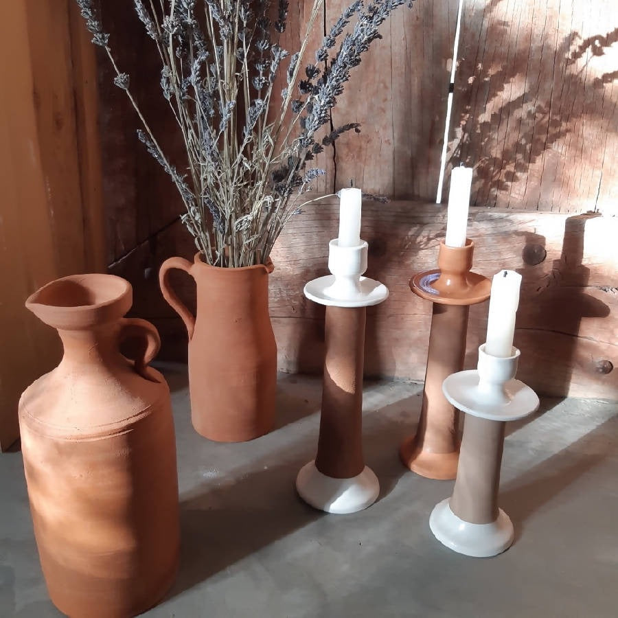 Leather-wrapped candle holders grouped with terracotta vessels and dried lavender in a rustic room