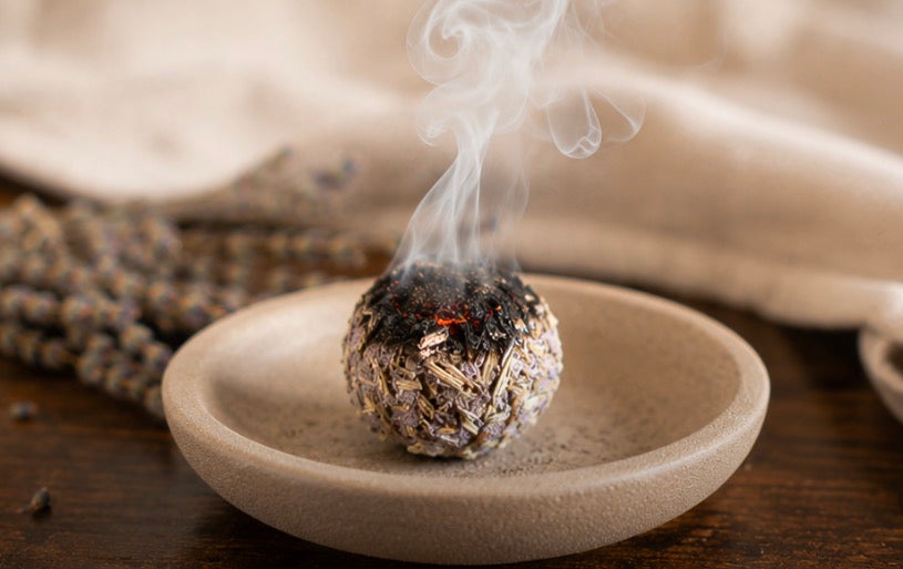 A lavender smudge bomb burning in a shallow ceramic dish with smoke rising