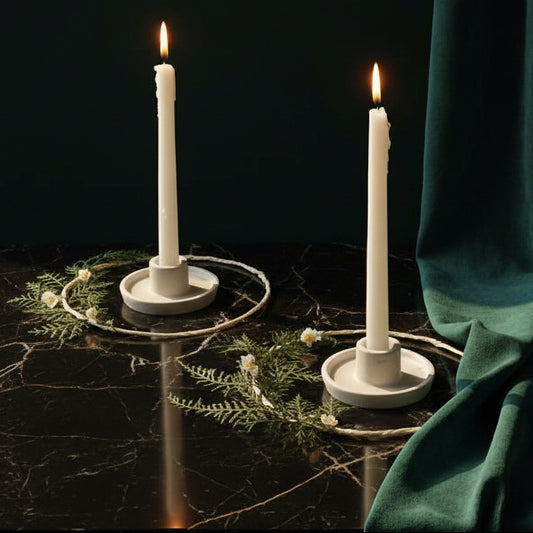 Two white Whirl candle holders with lit taper candles on dark marble