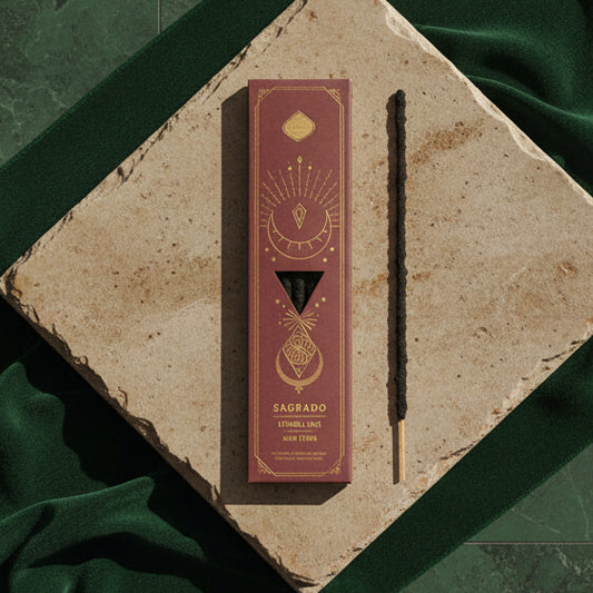The cocoa-brown Sagrado Divine Encounter box on a stone tile over green velvet, one black stick beside it.