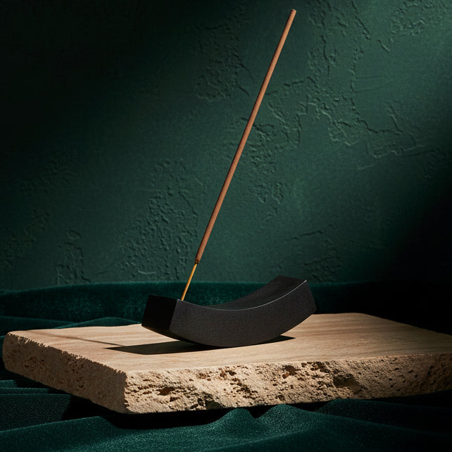 Black onyx Curve incense holder on a travertine slab, incense stick burning upright