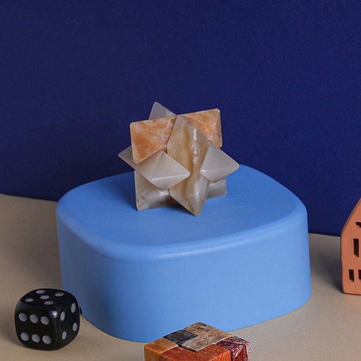 Assembled burr star puzzle in cream and peach-toned stone displayed on a blue plinth