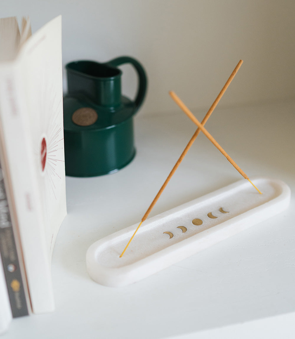 Moon phase marble incense holder with two incense sticks crossed, on a white shelf