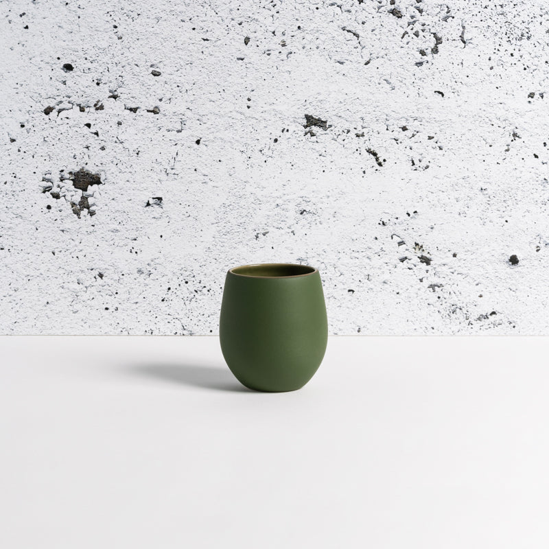 Green Epa stoneware cup against a speckled white plaster wall