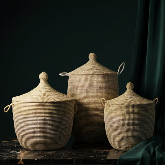 Three handwoven two-tone baskets with lids in graduated sizes on dark marble