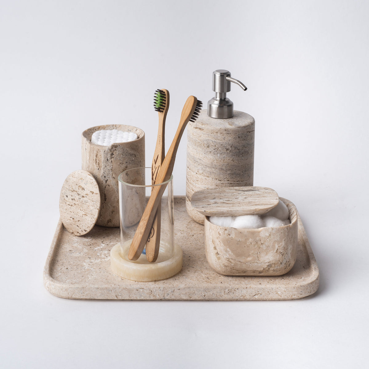 Travertine tray holding a matching soap dispenser, toothbrush cup and lidded jars