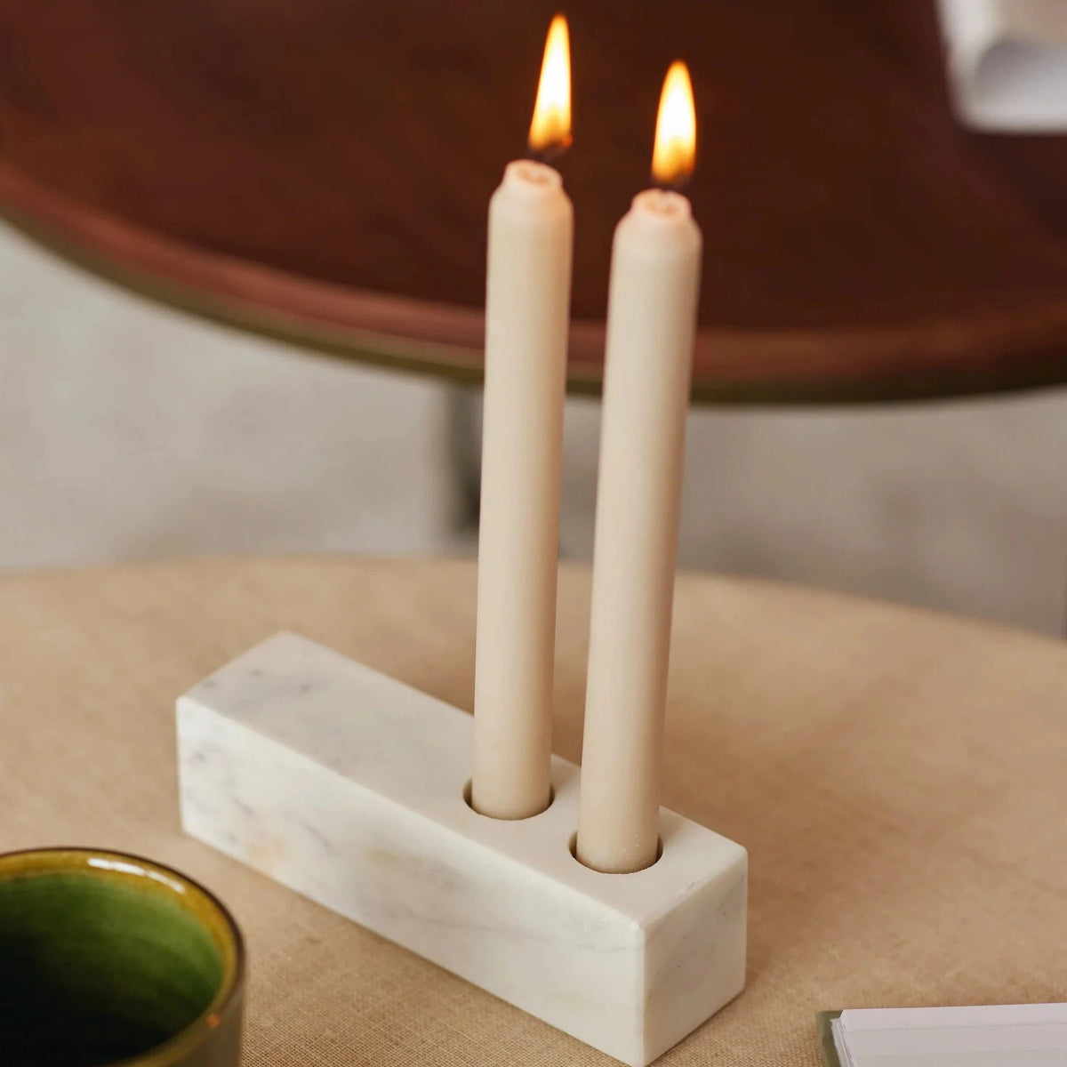 Marble candle holder with two lit taper candles on a side table