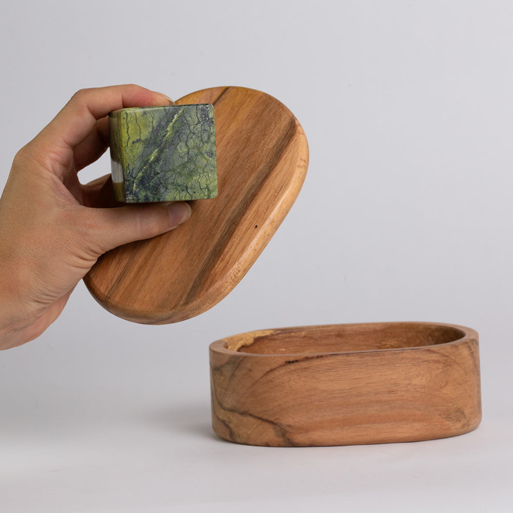 Hand lifting the wooden lid of the oval jewel box, showing the hollow base below
