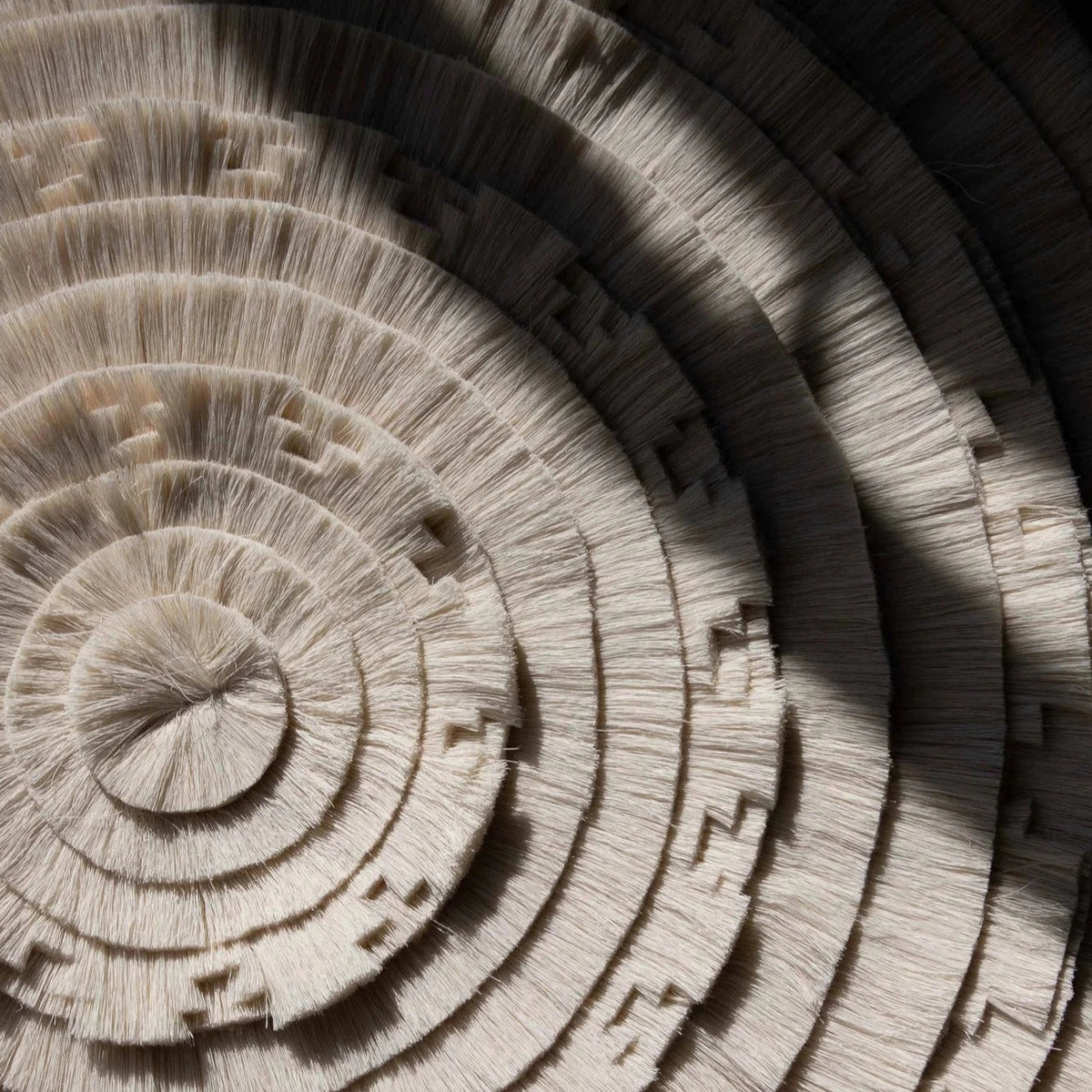 Close detail of the tapestry's concentric cotton fringe rings and stepped motifs